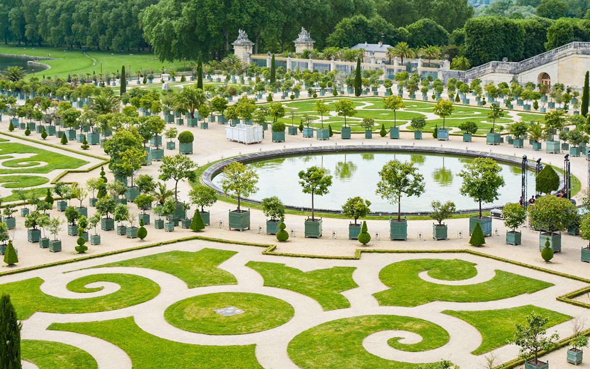 Palace of Versailles garden with ornate hedges and central fountain.