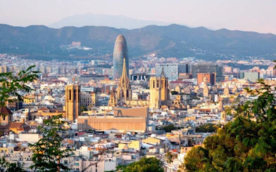 Barcelona skyline featuring Sagrada Familia and Torre Glòries with mountains in the background.