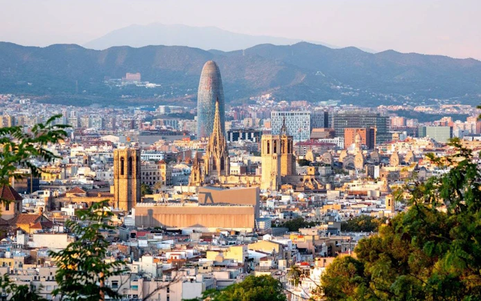 Barcelona skyline featuring Sagrada Familia and Torre Glòries with mountains in the background.