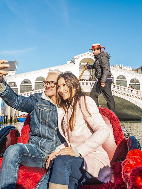 Couple taking selfie on gondola near Rialto Bridge, Venice.