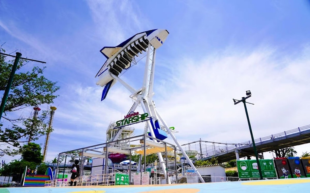 Looping starship ride at Yomiuriland amusement park in Tokyo against a clear sky.