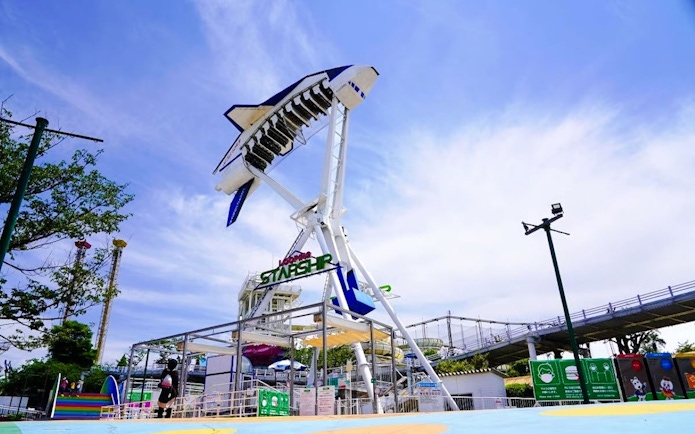 Looping starship ride at Yomiuriland amusement park in Tokyo against a clear sky.