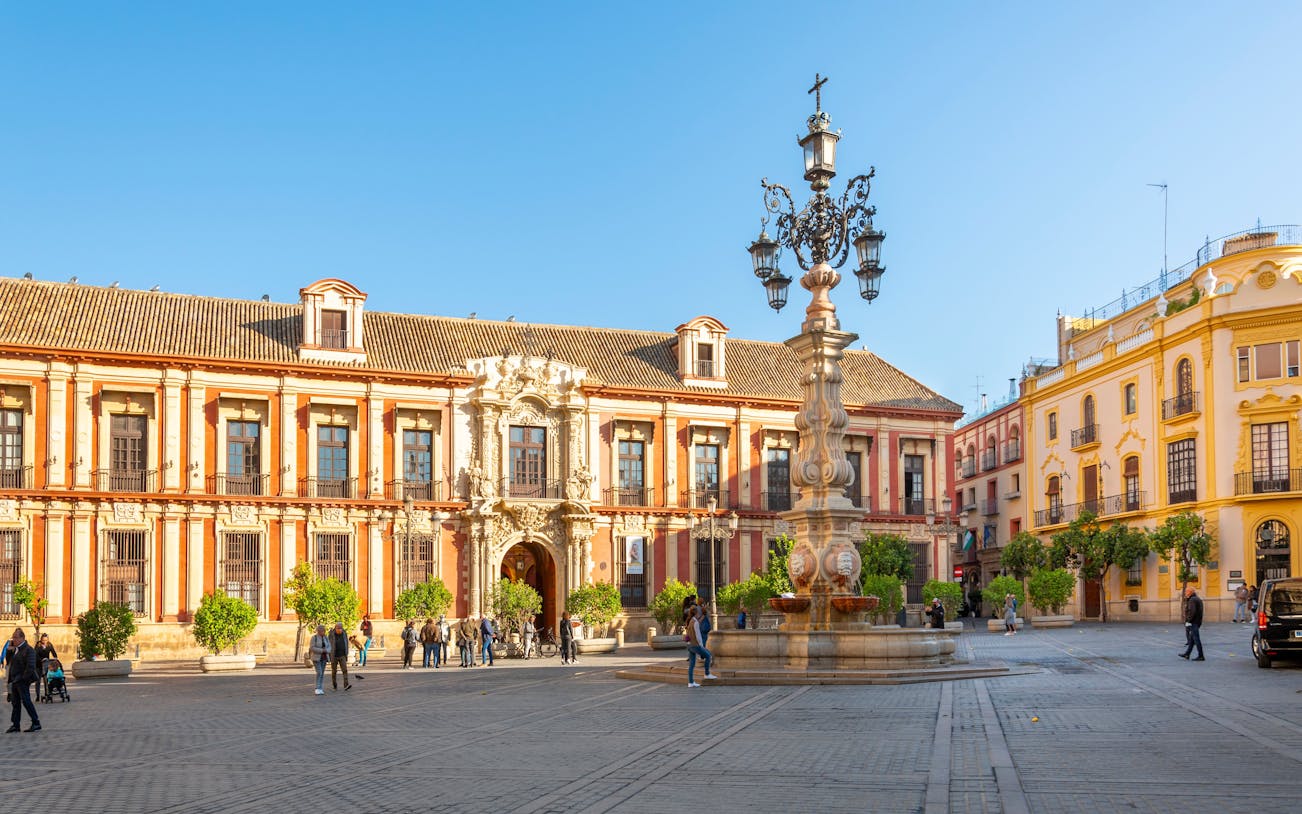 Plaza Virgen de los Reyes in Seville with tourists near historic buildings and ornate fountain.