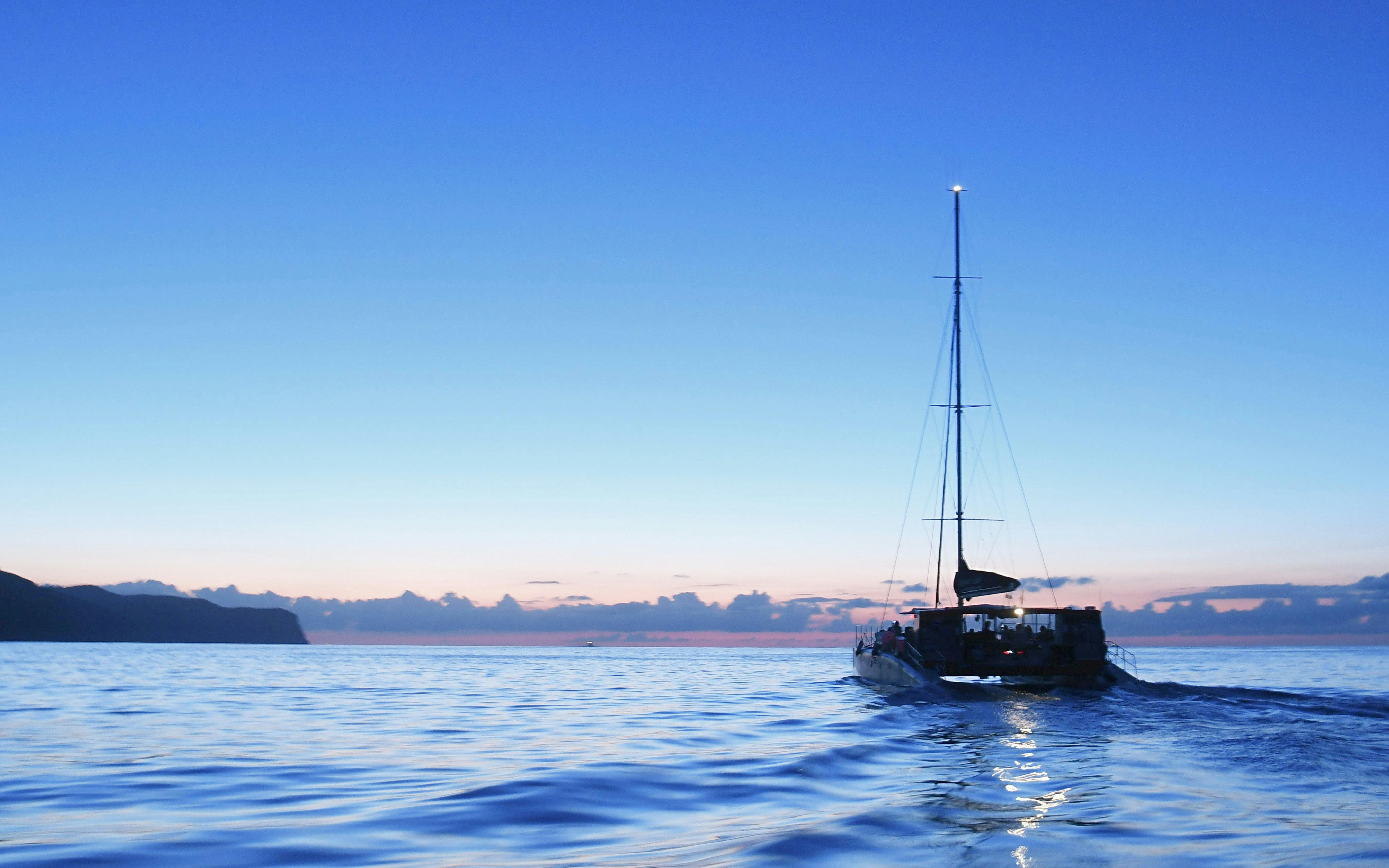 Catamaran sailing at sunrise in Mallorca with distant coastline.