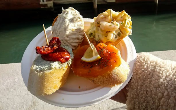 Venetian cicchetti with seafood and toppings on a plate by a canal during Venice street food tour.
