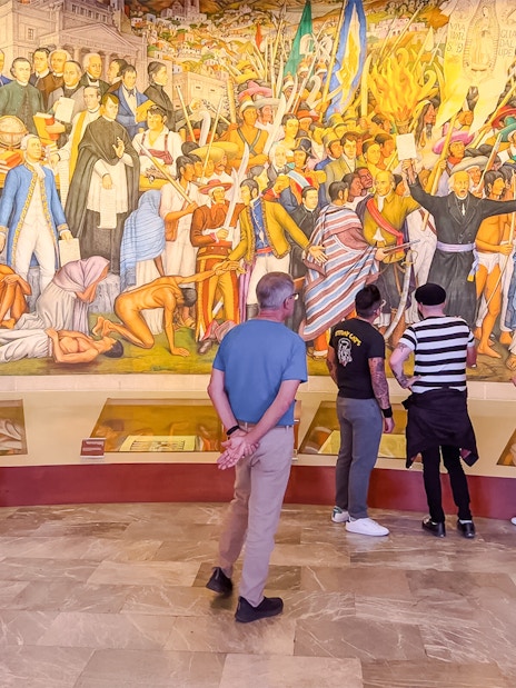Visitors viewing a vibrant mural at the Anthropology Museum in Mexico City.
