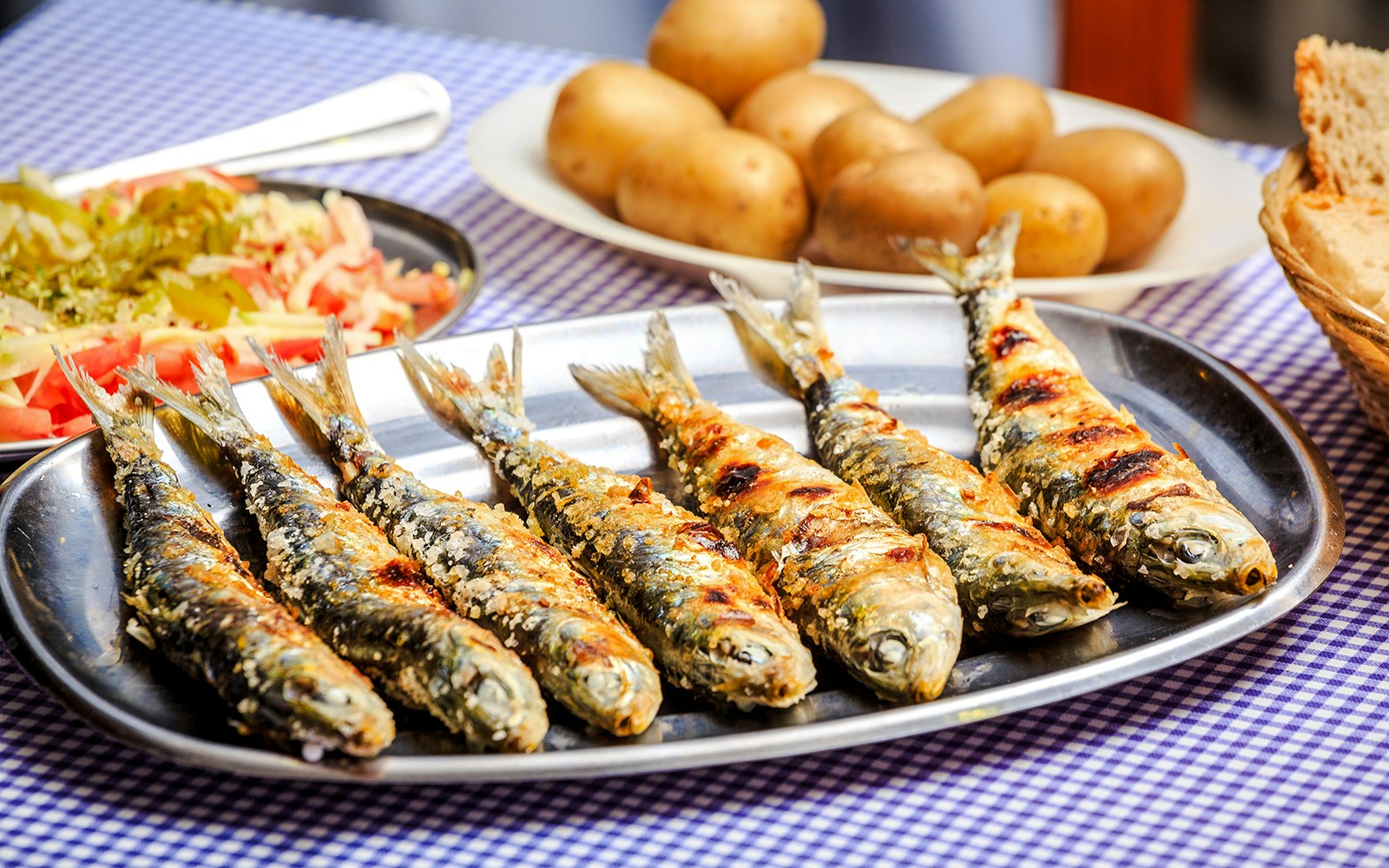 Grilled sardines on a platter with potatoes and salad.