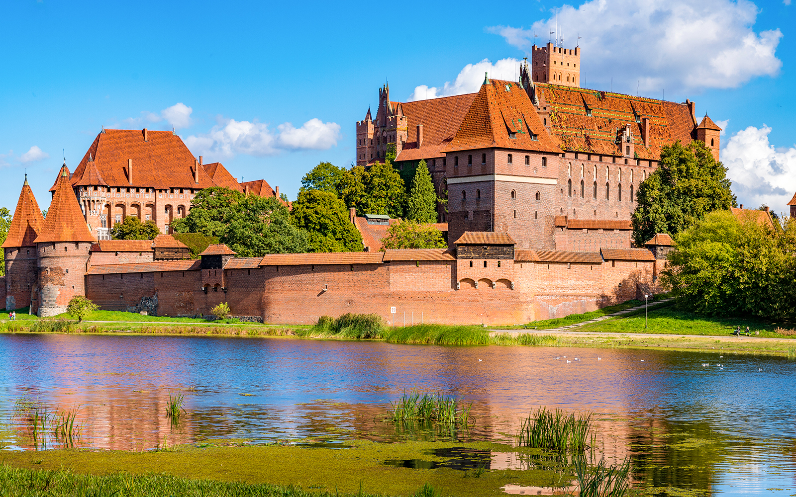 Malbork Castle with red brick walls and towers reflected in a river, Poland.