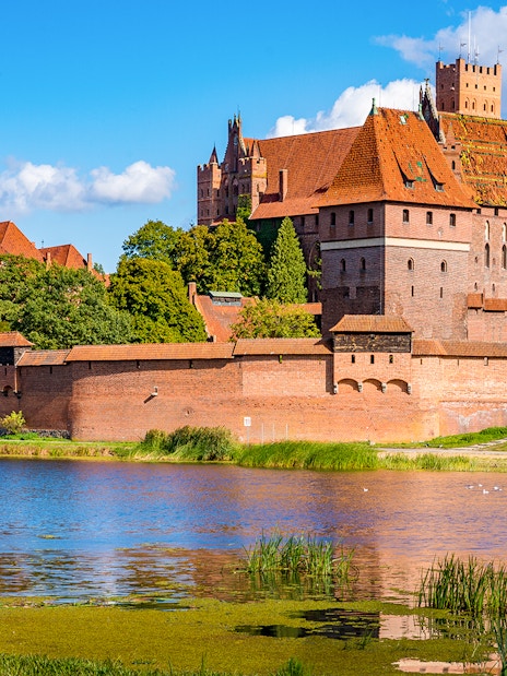 Malbork Castle with red brick walls and towers reflected in a river, Poland.