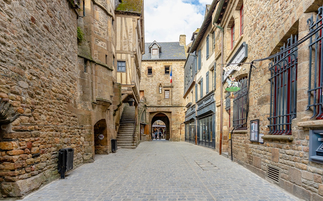 Narrow cobblestone street in Le Mont Saint Michel with historic stone buildings.
