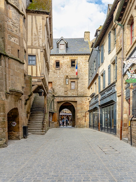 Narrow cobblestone street in Le Mont Saint Michel with historic stone buildings.