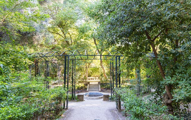Pathway through lush garden with metal archway on Acropolis Guided Bike Tour.
