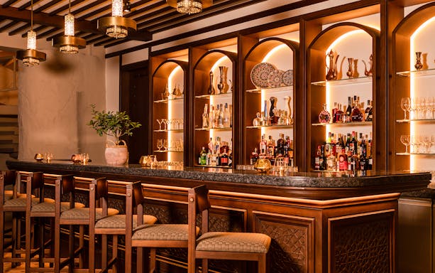 Bar area with wooden decor and shelves of drinks at Al Hadheerah Restaurant, Bab Al Shams desert resort.