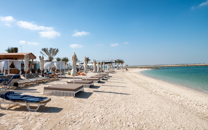 Sun loungers and cabanas on Yas Island beach, Abu Dhabi, with clear blue water.