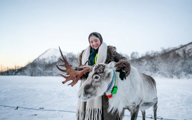 Guest interacting with a reindeer during a Sámi culture experience in snowy landscape.