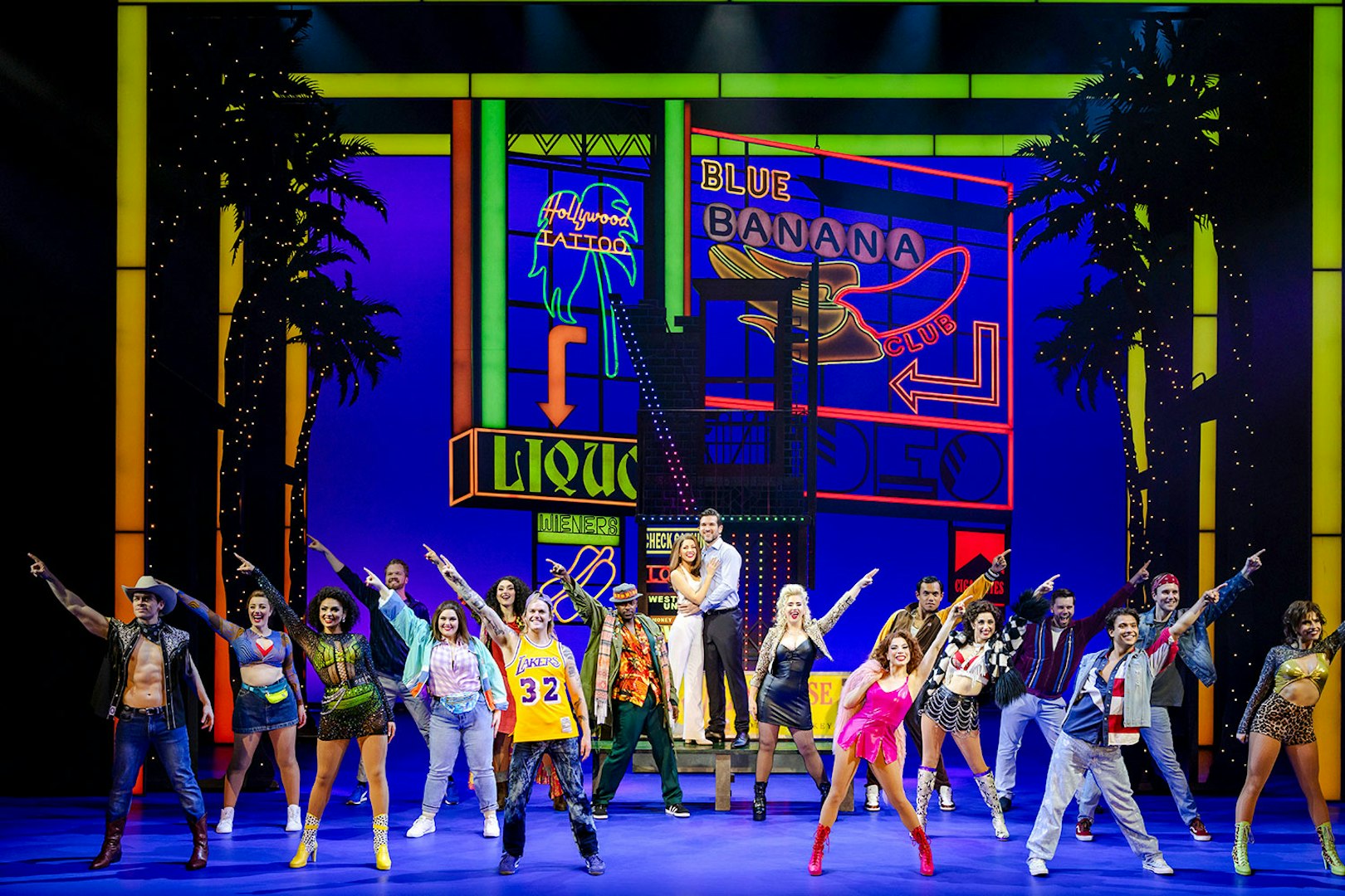 Cast performing a scene from Pretty Woman The Musical with colorful neon signs in the background.