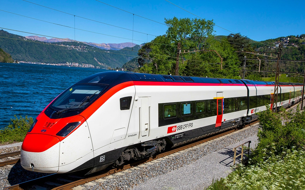 Train traveling along a scenic route near a lake, connecting Geneva Airport and Geneva Train Station.