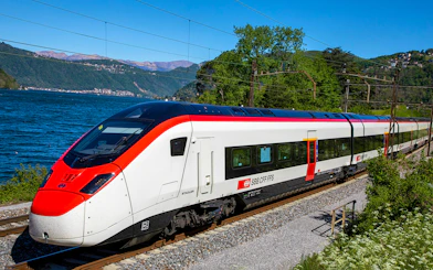 Train traveling along a scenic route near a lake, connecting Geneva Airport and Geneva Train Station.