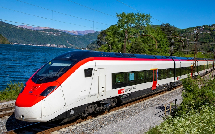 Train traveling along a scenic route near a lake, connecting Geneva Airport and Geneva Train Station.