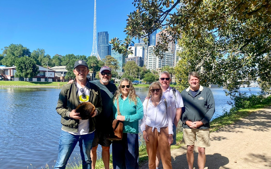 Group enjoying Melbourne Sports Guided Walking Tour by the river with city skyline.