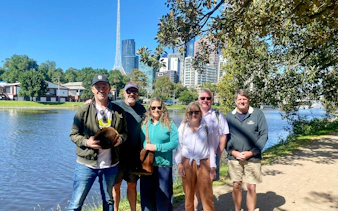 Group enjoying Melbourne Sports Guided Walking Tour by the river with city skyline.