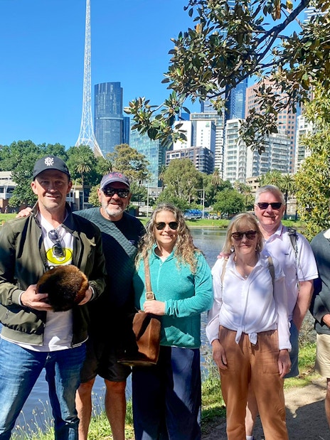 Group enjoying Melbourne Sports Guided Walking Tour by the river with city skyline.