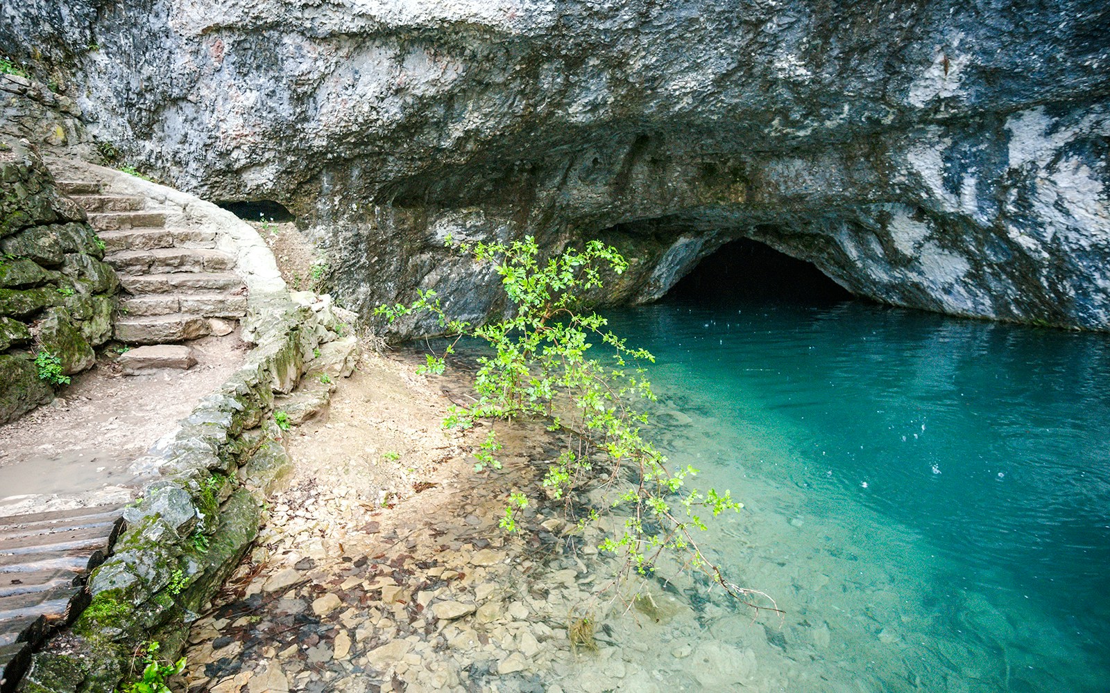 Stone steps leading to the entrance of Green Cave, Croatia, with clear blue water.