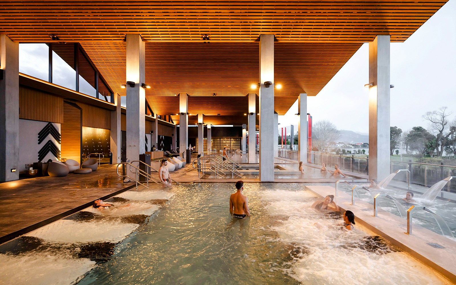 Visitors enjoying thermal pools at Wai Ariki Hot Springs & Spa, with modern architecture and scenic views.