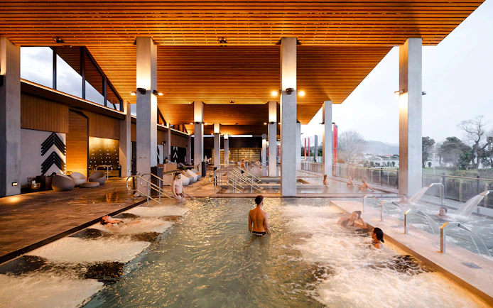 Visitors enjoying thermal pools at Wai Ariki Hot Springs & Spa, with modern architecture and scenic views.