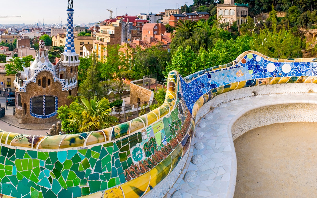 Serpentine Bench with mosaic tiles in Parc Guell, Barcelona, overlooking cityscape.