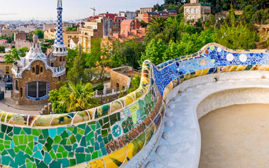 Serpentine Bench with mosaic tiles in Parc Guell, Barcelona, overlooking cityscape.