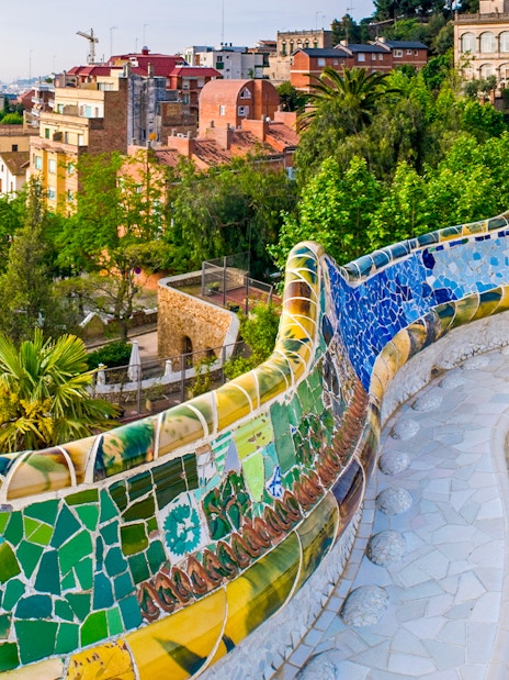 Serpentine Bench with mosaic tiles in Parc Guell, Barcelona, overlooking cityscape.