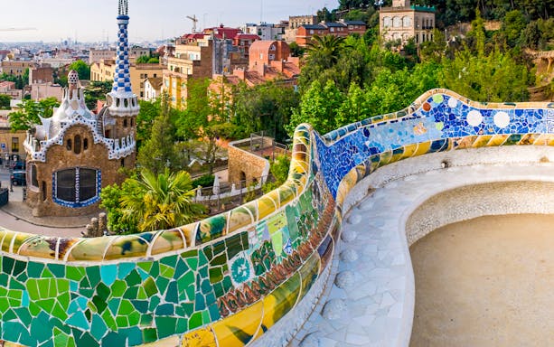Serpentine Bench with mosaic tiles in Parc Guell, Barcelona, overlooking cityscape.