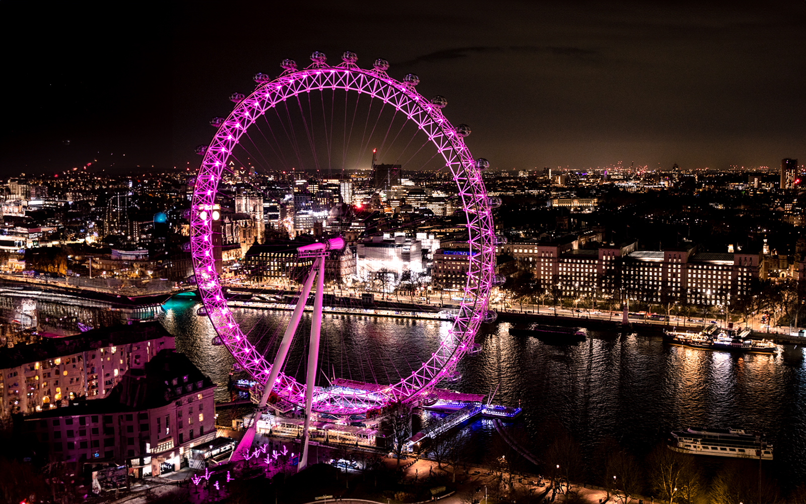 London Eye illuminated at night, overlooking the Thames River and cityscape.