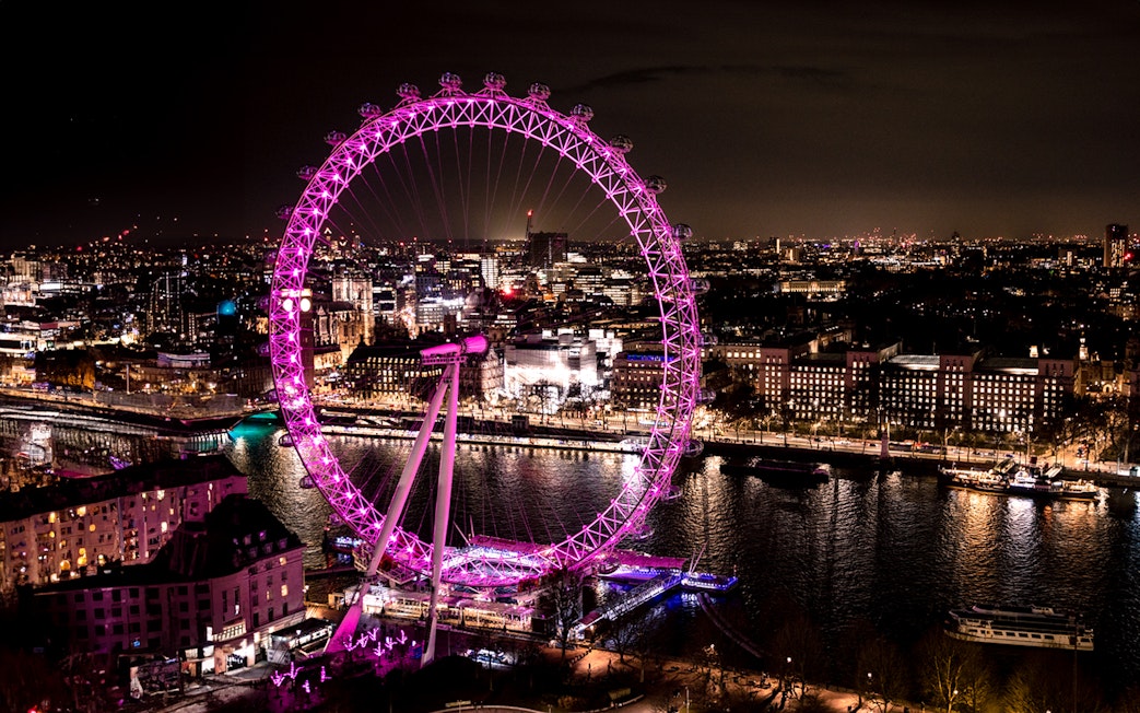 London Eye illuminated at night, overlooking the Thames River and cityscape.