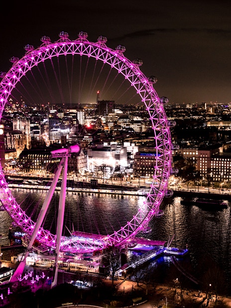 London Eye illuminated at night, overlooking the Thames River and cityscape.