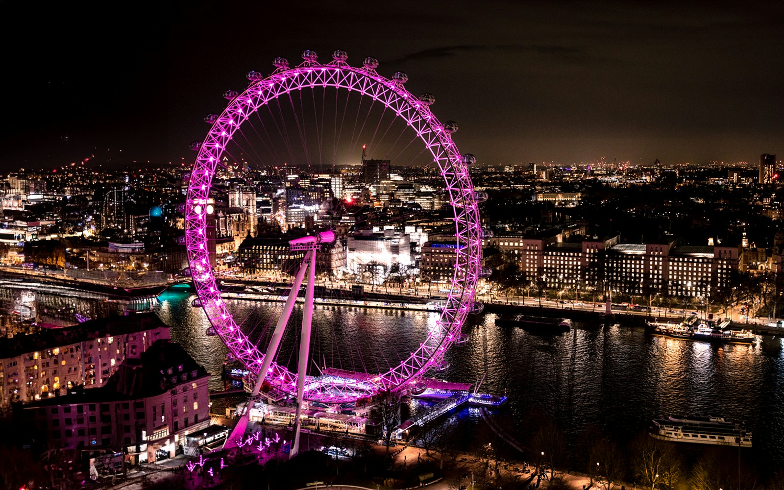 London Eye illuminated at night, overlooking the Thames River and cityscape.
