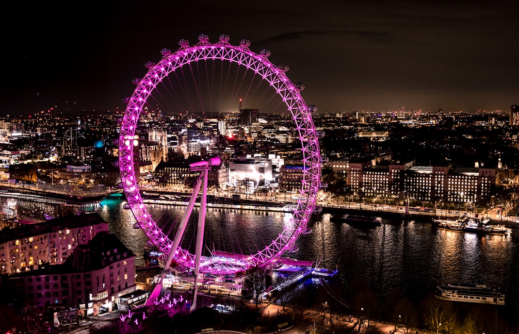 London Eye illuminated at night, overlooking the Thames River and cityscape.