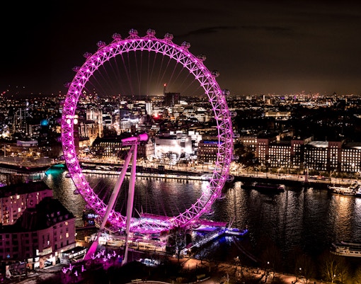London Eye illuminated at night, overlooking the Thames River and cityscape.