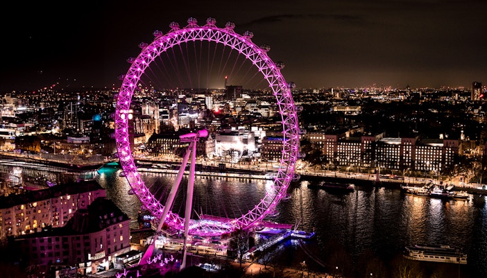 London Eye illuminated at night, overlooking the Thames River and cityscape.