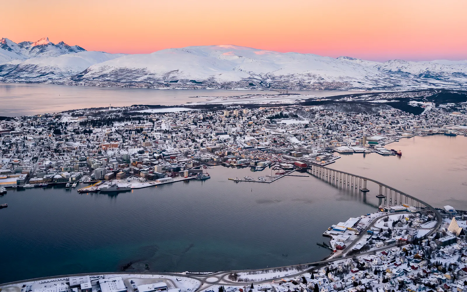Aerial view of Tromsø cityscape with snow-covered mountains and fjord in the Arctic landscape.