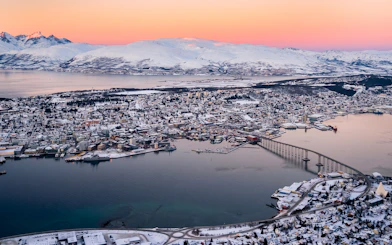 Aerial view of Tromsø cityscape with snow-covered mountains and fjord in the Arctic landscape.