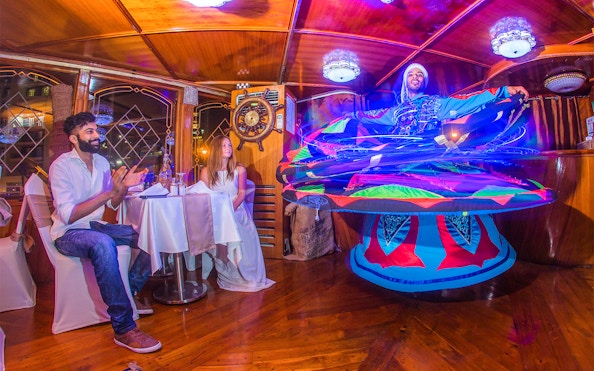 Dancers perform traditional Tanoura dance on Dubai Marina dhow cruise with guests dining.