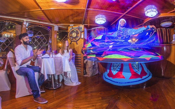 Dancers perform traditional Tanoura dance on Dubai Marina dhow cruise with guests dining.