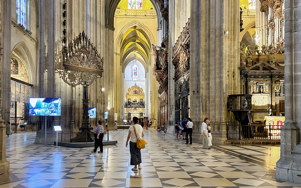 Seville Cathedral interior with visitors walking through the ornate nave.