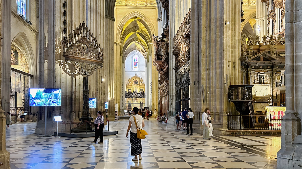 Seville Cathedral interior with visitors walking through the ornate nave.