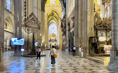Seville Cathedral interior with visitors walking through the ornate nave.