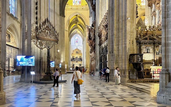 Seville Cathedral interior with visitors walking through the ornate nave.