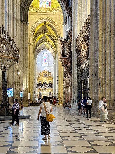 Seville Cathedral interior with visitors walking through the ornate nave.