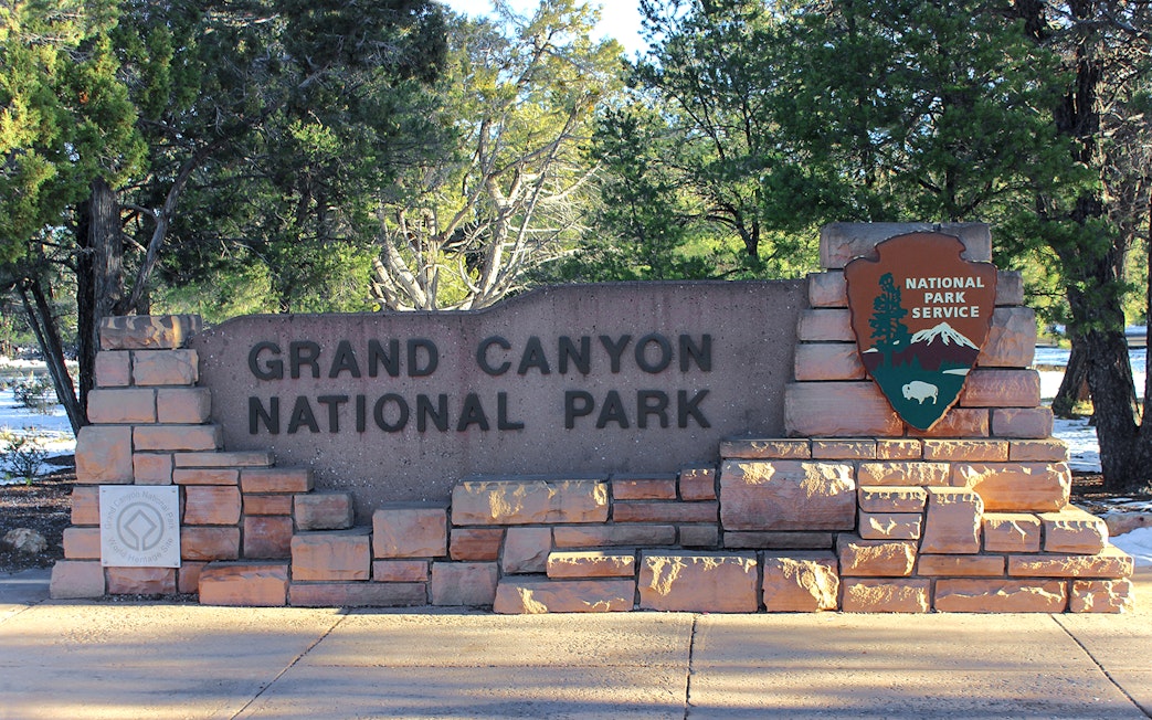 Grand Canyon National Park entrance sign surrounded by trees.